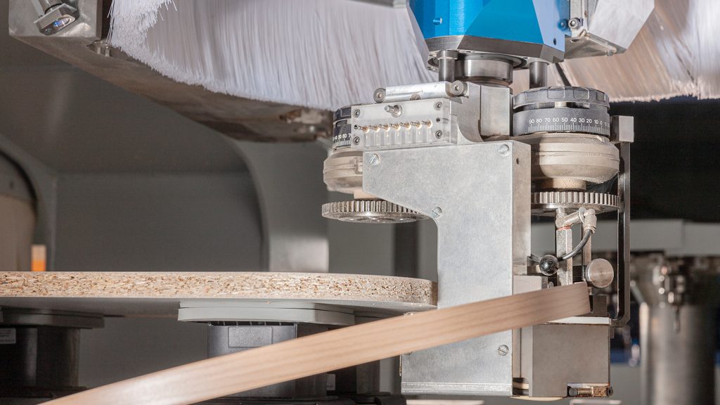 Close-up of woodgrain edge banding being applied to a furniture panel — HOMAG application example